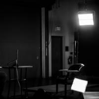 一个人坐在演播室里，开着演播室的灯，坐着做一个虚拟的演讲